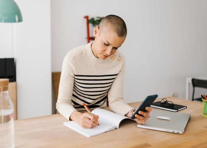 Mid adult woman taking notes while checking some information on mobile phone